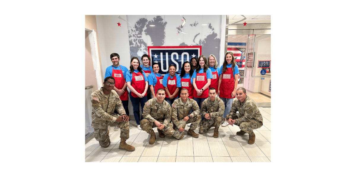 Affleck & Gordon team volunteers at the airport USO, posing with service members in front of a USO sign.